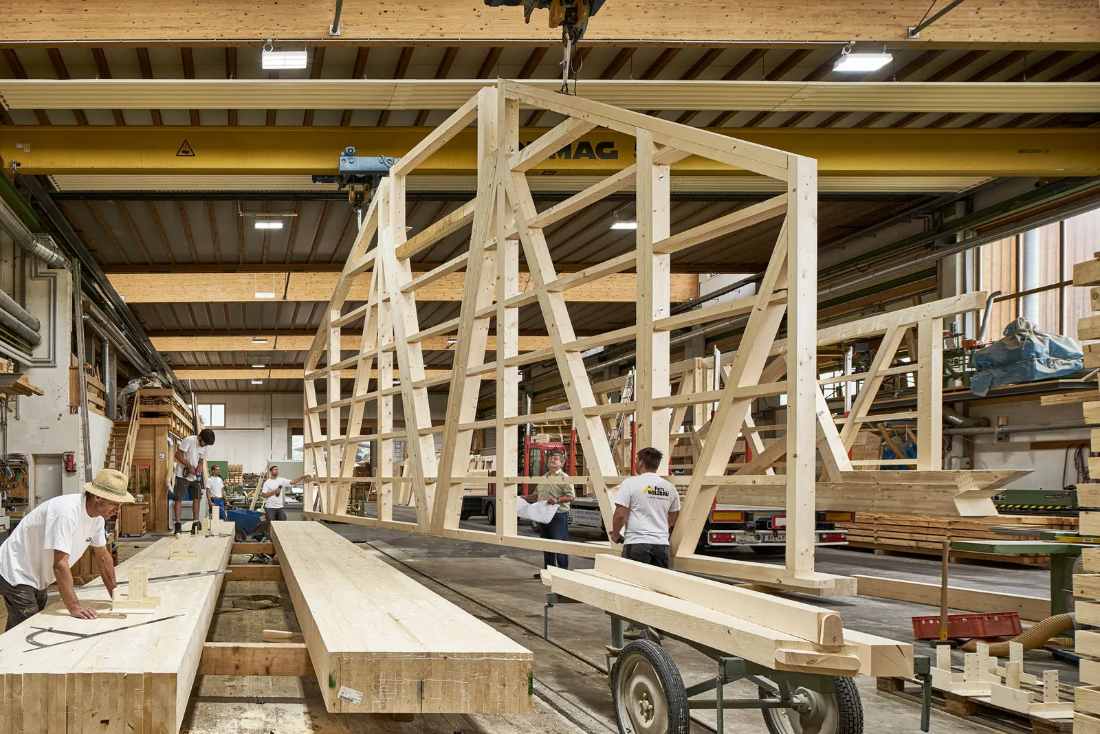 Abbundhalle mit gelbem Brückenkran, ein Fachwerk-Element hängt am Haken